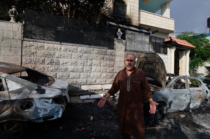 A man stands in front of burnt cars in a West Bank village attacked by Jewish settlers