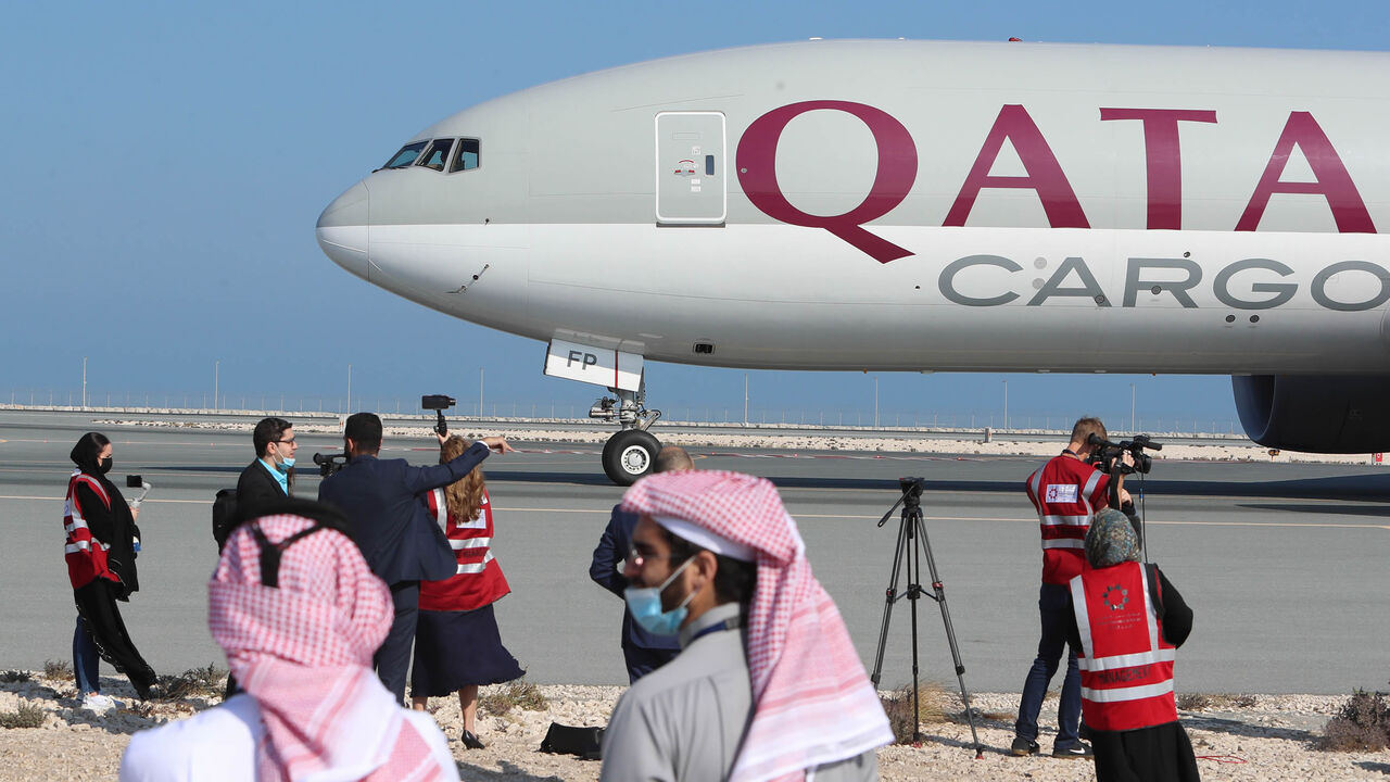 Reporters gather near a Qatar Airways cargo airplane on the tarmac of Hamad International Airport, as the first commercial flight to Saudi Arabia in three and a half years following a Gulf diplomatic thaw prepares for take-off, Doha, Qatar, Jan. 11, 2021. 