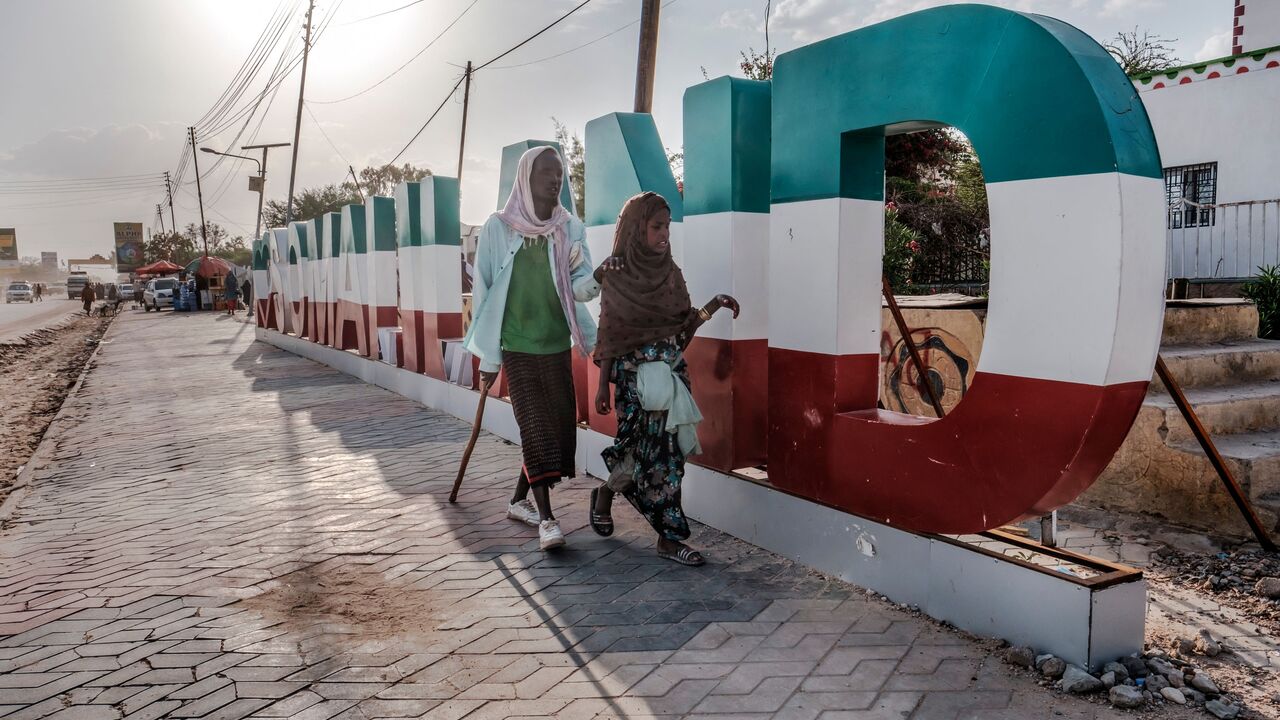 A blind man guided by a girl walk in front of a sign, in the city of Hargeisa, Somaliland, on September 16, 2021. - For 30 years, Somaliland has tried unsuccessfully to convince the world of its case for statehood, holding democratic elections and avoiding the anarchy that engulfed the rest of Somalia. (Photo by EDUARDO SOTERAS / AFP) (Photo by EDUARDO SOTERAS/AFP via Getty Images)