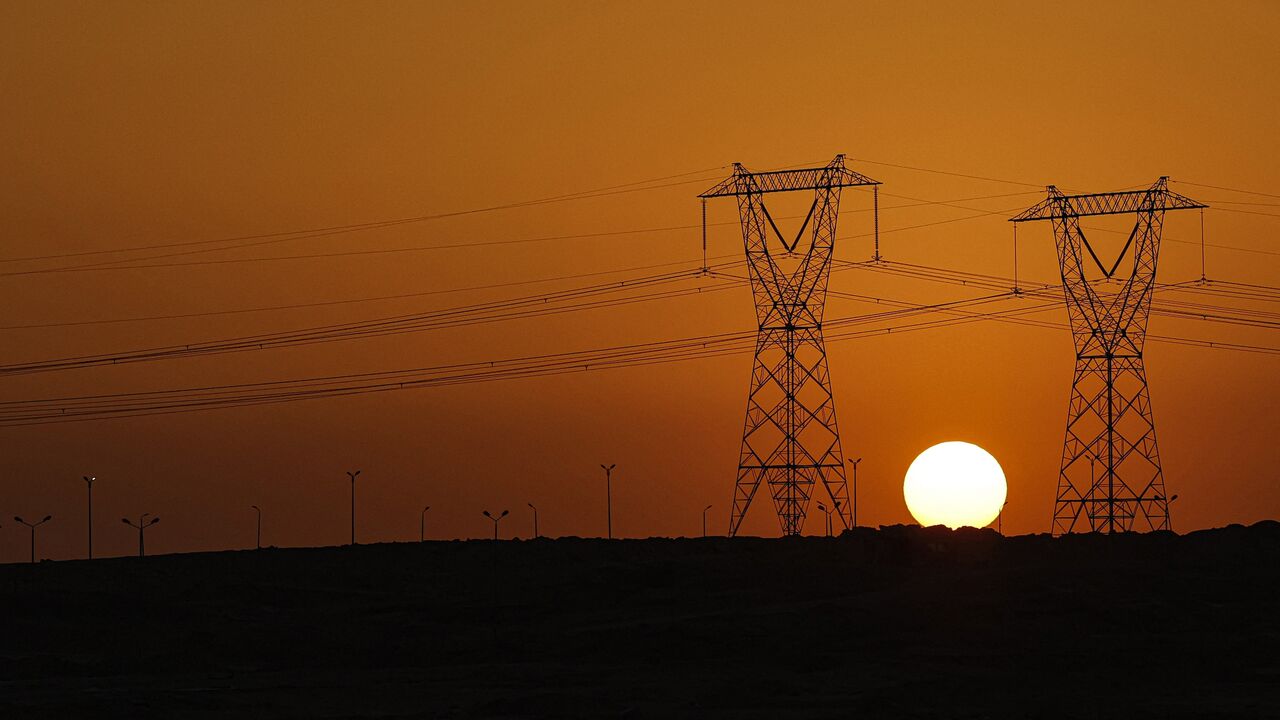 The sun sets behind high voltage transmission towers (electricity pylons) along a highway in El-Shorouk, a satellite city about 47 kilometers outside the city center of Cairo, on July 24, 2023. 