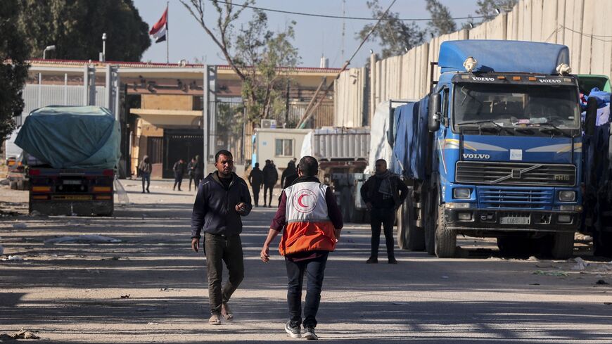 People walk past trucks carrying humanitarian aid that entered Gaza by truck through the Kerem Shalom (Karm Abu Salem) border crossing.