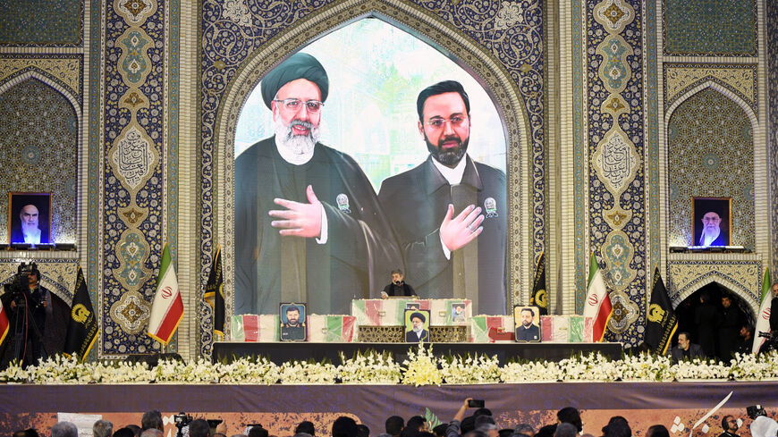 An Iranian man reads a prayer over the coffins of late president Ebrahim Raisi (portrait top L) and late governor of Iran's East Azerbaijan Province Malik Rahmati (portrait top R) during a funeral ceremony at the Imam Reza shrine, in the city of Mashhad, on May 23, 2024.