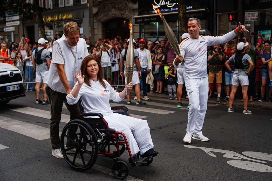 TOPSHOT - Agence France Presse (AFP) Lebanese photographer Christina Assi (C) helped by AFP video journalist Dylan Collins (L), waves after receiving the Olympic flame during the Olympic Torch Relay in Vincennes, near Paris, on July 21, 2024, ahead of the Paris 2024 Olympic Games. AFP journalists Christina Assi and Dylan Collins were injured in an attack by an Israeli tank on a group of journalists in southern Lebanon on October 13, 2023. (Photo by Dimitar DILKOFF / AFP) (Photo by DIMITAR DILKOFF/AFP via Ge