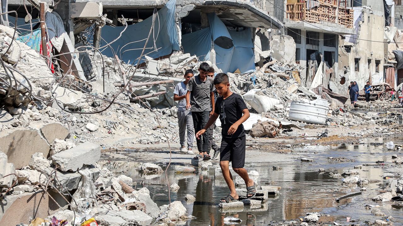 Boys walk on dry bricks to traverse a puddle of sewage water past mounds of trash and rubble along a street in the Jabalia camp for Palestinian refugees, northern Gaza Strip, August 14, 2024.